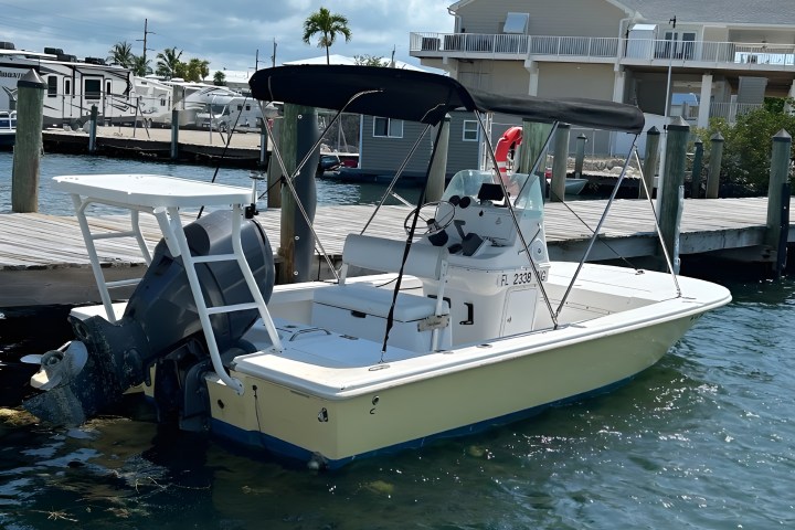 Small motorboat docked at a pier with a house and clear sky in the background.