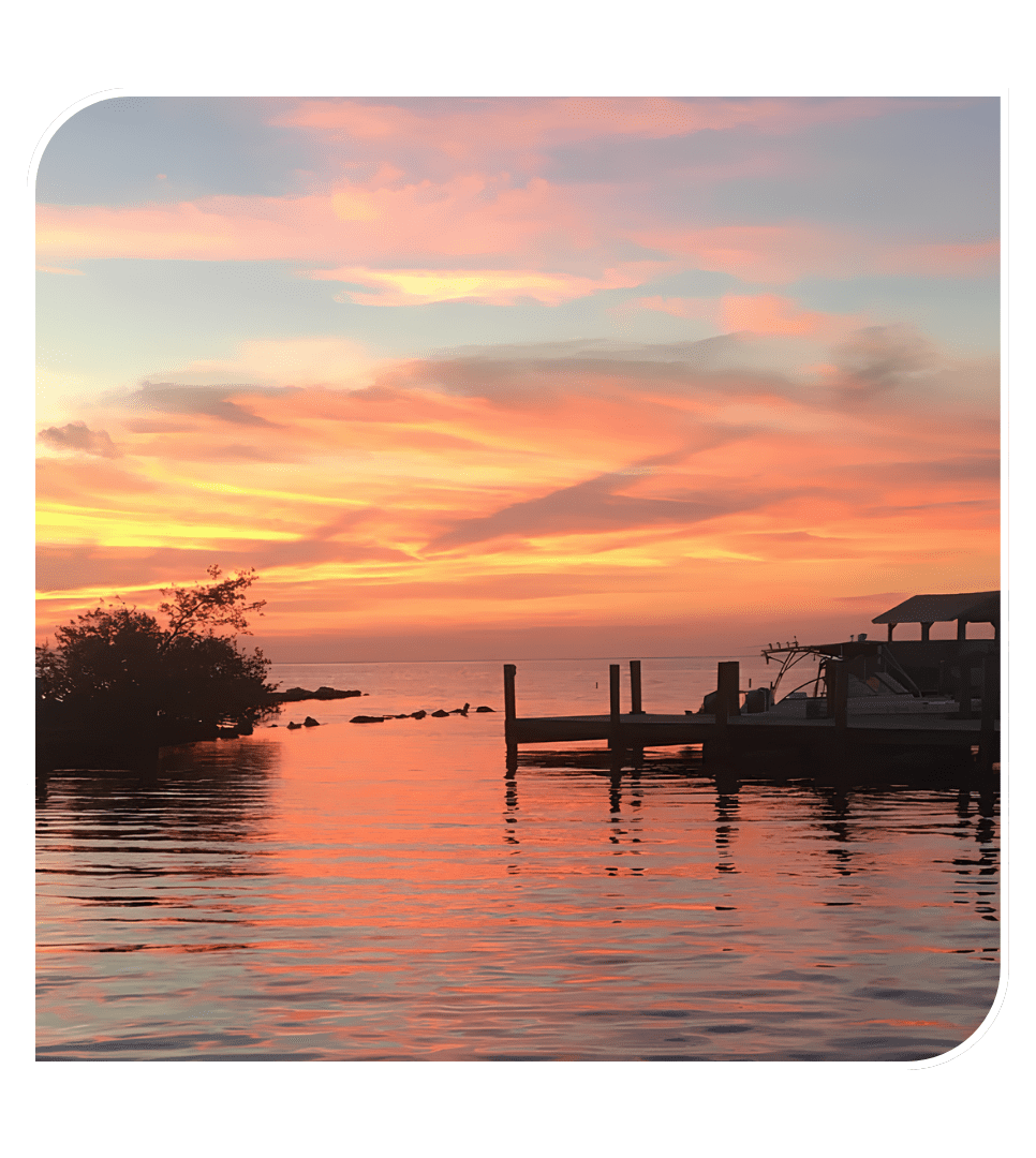 Sunset over water with orange and pink clouds, silhouette of a dock and boat.