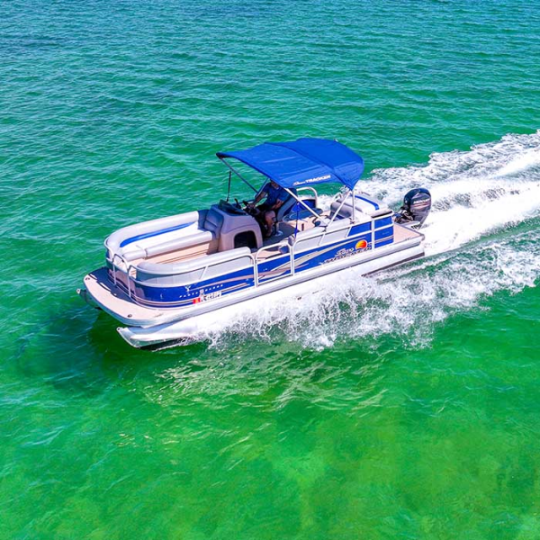 A pontoon boat with a blue canopy cruising on clear green water.