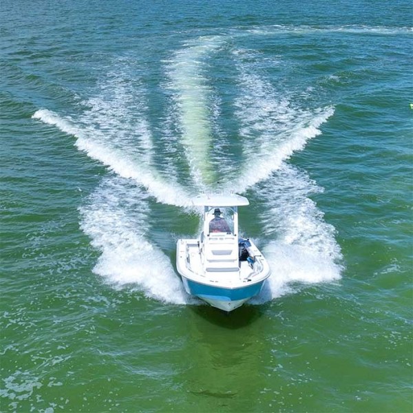 Boat moving on green water, creating wake patterns behind it on a sunny day.