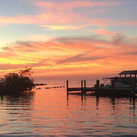 Boats docked at sunset with vibrant orange and pink sky reflecting on water.
