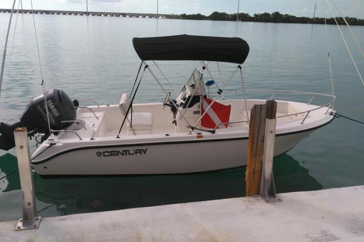 Small motorboat docked at a pier on calm water with distant bridge.