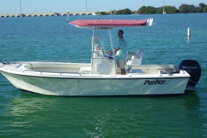 Man stands on a white boat with a red canopy on clear green water.